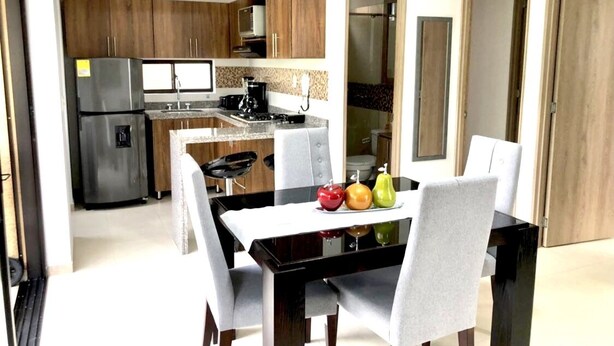 Een moderne keuken met houten kasten, een roestvrijstalen koelkast en een eethoek met een zwarte tafel en witte stoelen.