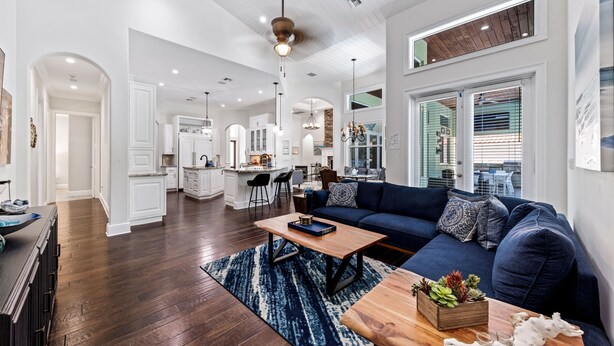 A spacious living area with a dark blue sofa, wooden coffee table, and a kitchen in the background.