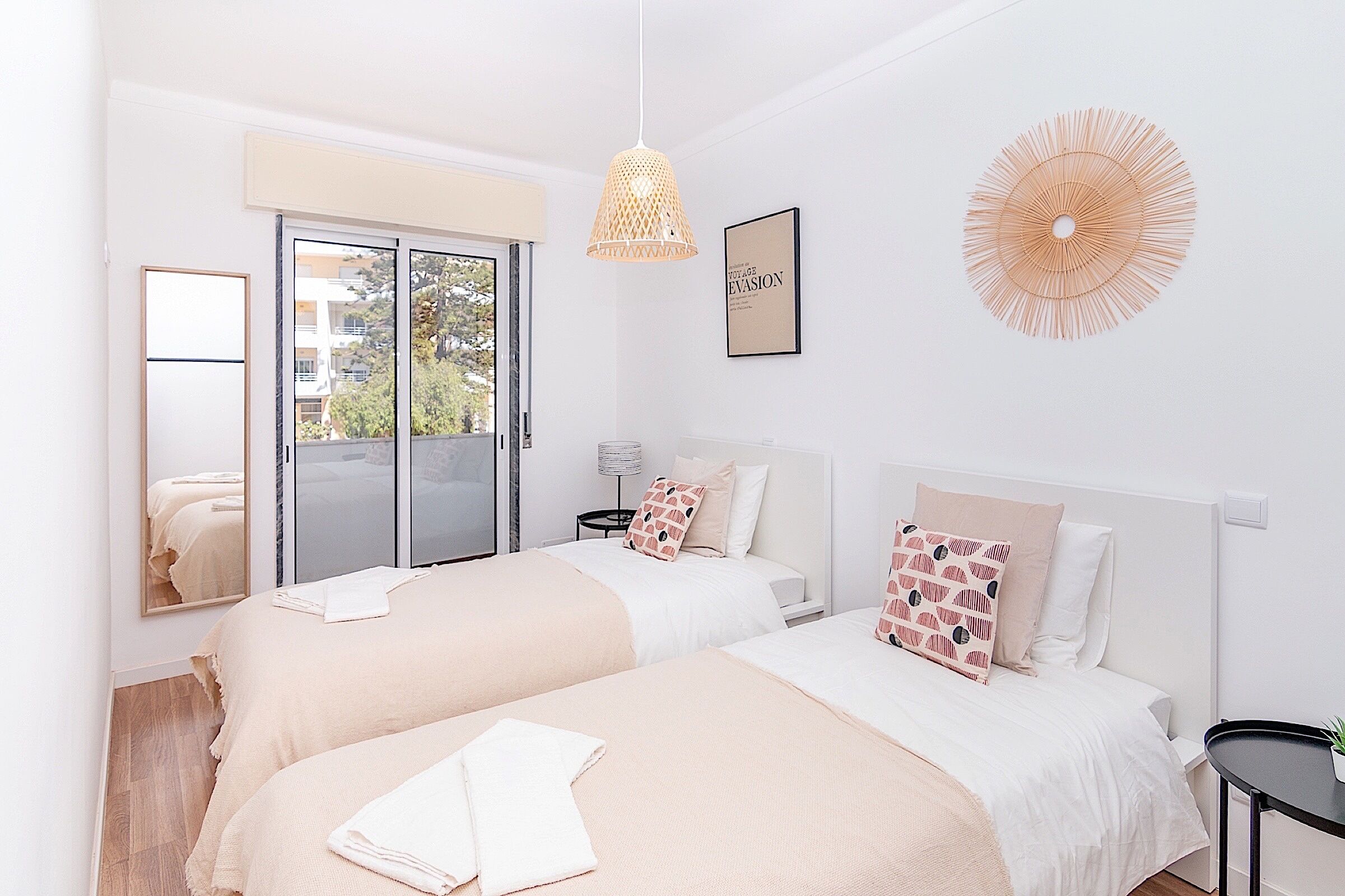 A modern bedroom with two beds, a large window, a ceiling fan, and a framed artwork.