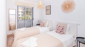 Una camera da letto moderna con due letti, una grande finestra, una ventola a soffitto e un'opera d'arte incorniciata.