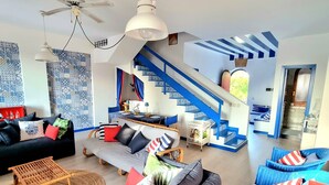 A spacious living area with a sofa, a coffee table, and a dining table set up. There is a staircase with blue accents leading to an upper level. - [SEA VIEW] On three floors with garden (Falerna Marina)
