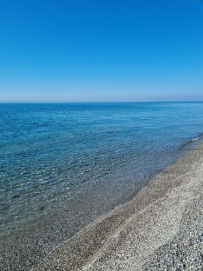 A clear view of a pebble beach leading to calm waters under a clear blue sky. - [OCEAN VIEW] Three-story home with a garden (Falerna Marina)