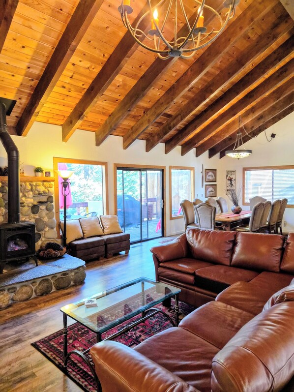 A spacious living room with a stone fireplace, leather sofas, a glass coffee table, and a high wooden ceiling.