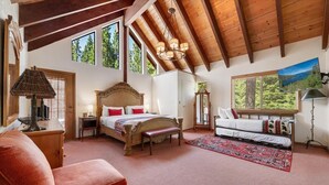 Ein geräumiges Schlafzimmer mit einem großen Bett, einer Bank, einem Sofa und Blick ins Freie durch ein Fenster.