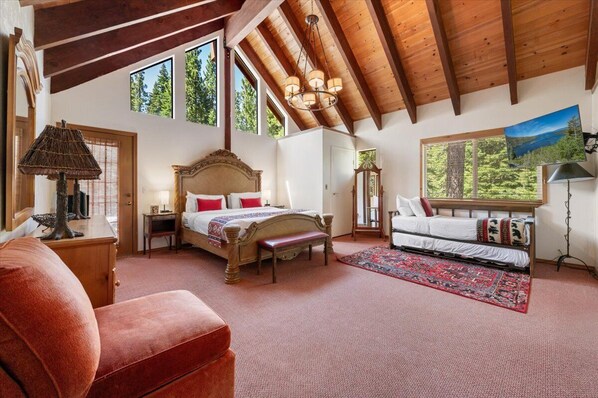 A spacious bedroom with a large bed, a bench, a sofa, and a view of the outdoors through a window.