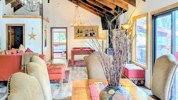 Ein gemütliches Wohnzimmer mit Holzbalkendecke, einem großen Tisch und bequemen Sitzgelegenheiten.