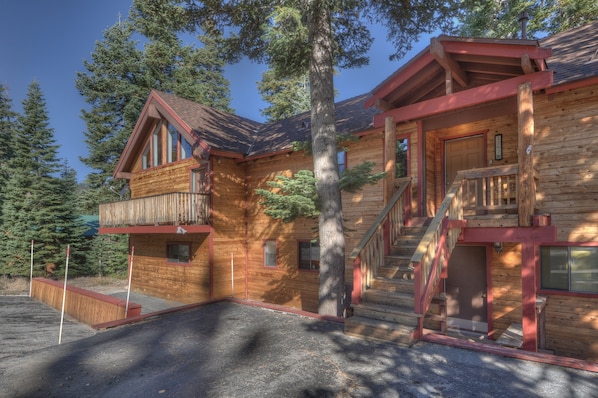 A log cabin with a balcony, a staircase, and a large tree in front.