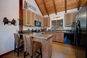 A kitchen with wooden cabinets, a black refrigerator, and a wooden island with two chairs.