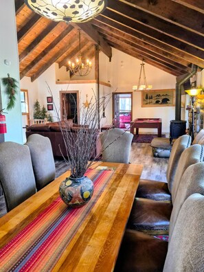 A spacious living area with a high ceiling, wooden beams, a fireplace, and a dining table with chairs.