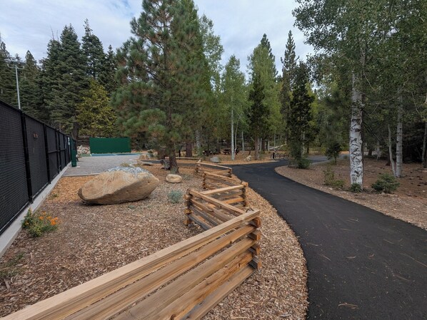 A paved path with wooden railings, surrounded by trees and a fenced area.