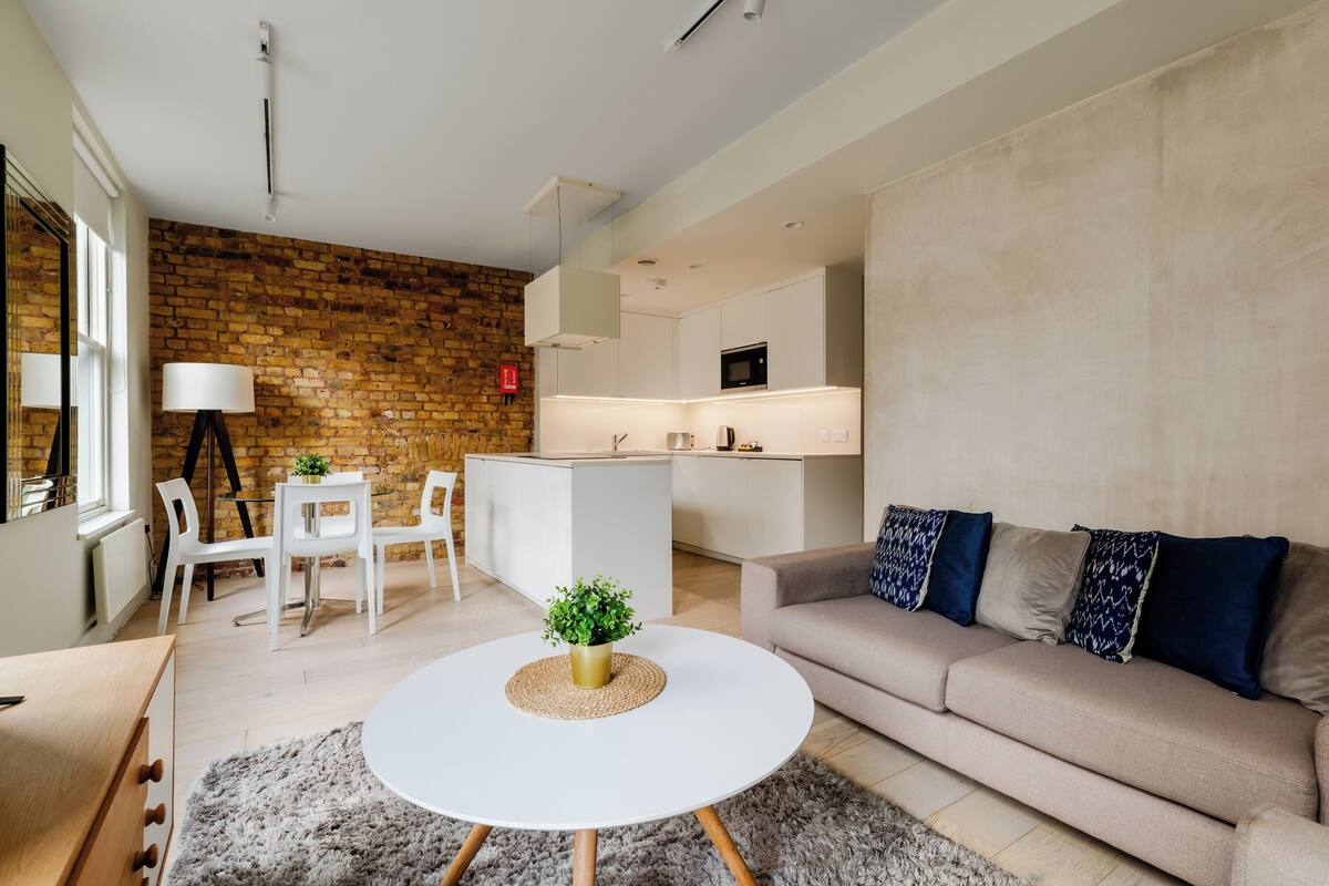 A modern living room with a round white coffee table, a beige sofa with patterned cushions, and a brick wall.