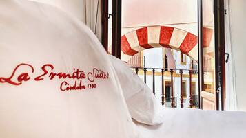 Une chambre d’hôtel avec un lit, une fenêtre donnant sur un bâtiment orné d’une arche à rayures rouges et blanches, et un oreiller blanc avec un motif imprimé.