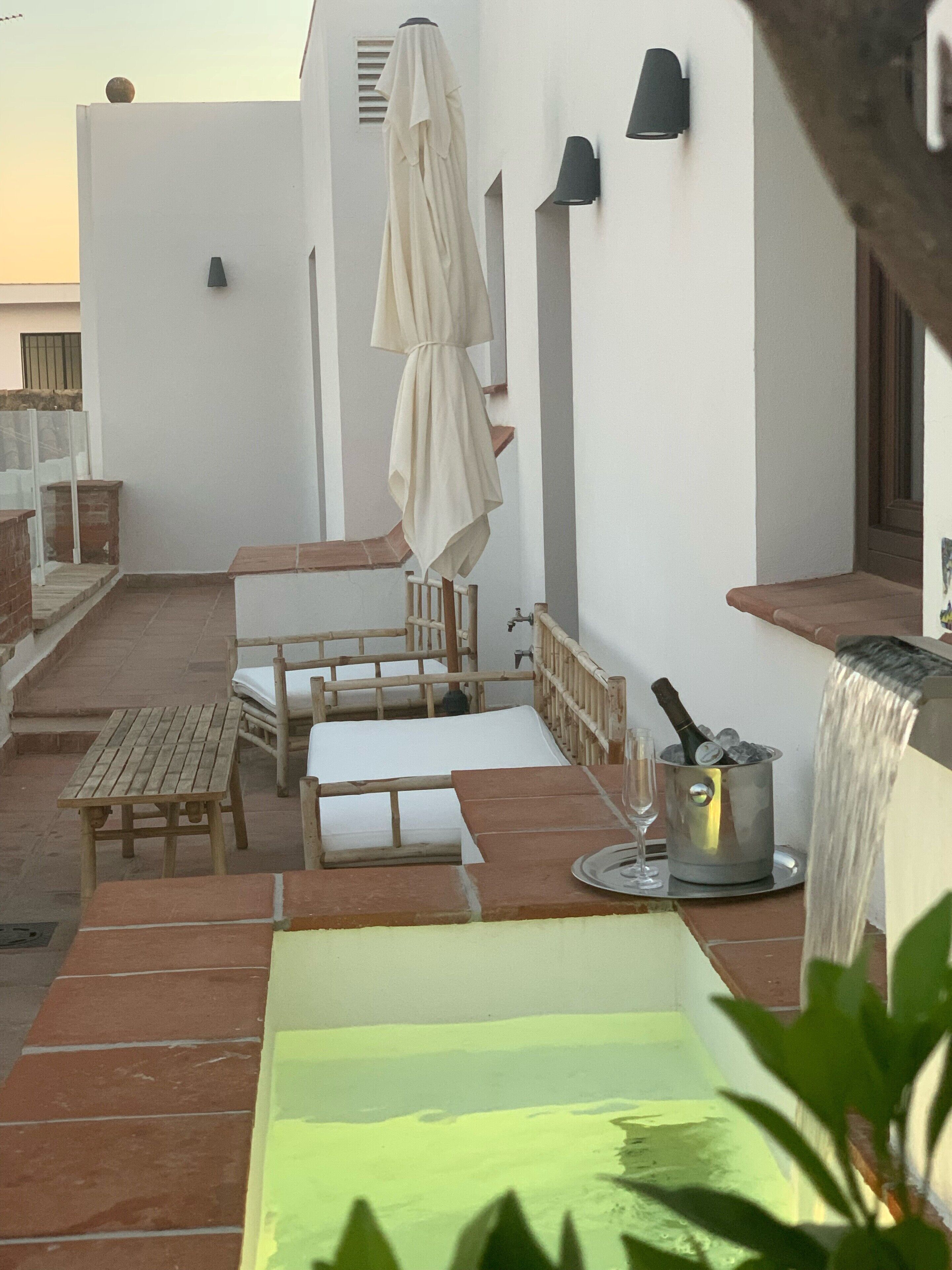 A rooftop terrace with a seating area, a table with a bottle of champagne, and a water feature.