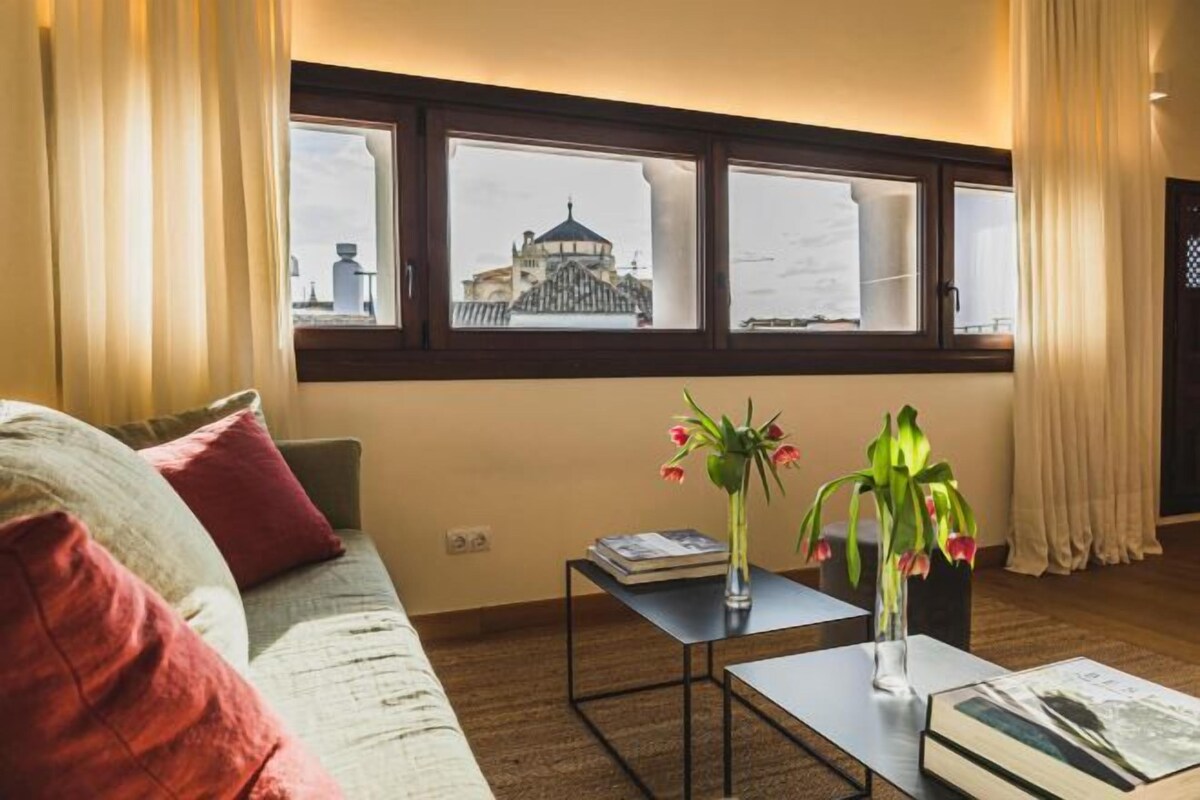 A living room with a sofa, a coffee table, and a view of a building through a window.