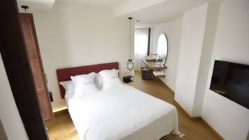 Un dormitorio con cama, suelo de madera, televisor y baño con lavamanos y espejo.