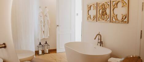 A modern bathroom with a freestanding bathtub, a toilet, and a sink. There are two wall-mounted light fixtures and a door leading to another room.