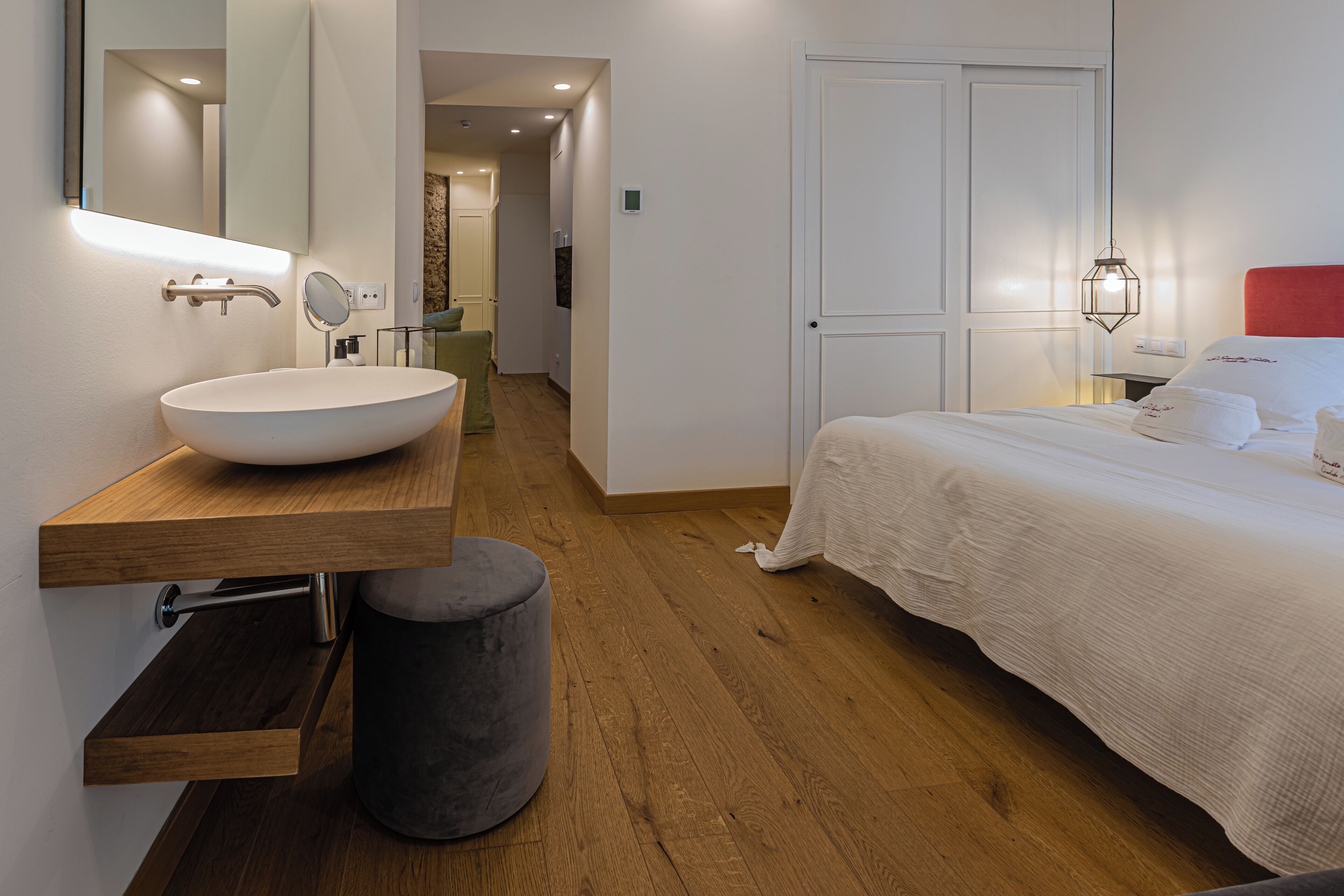 A modern bedroom with a large bed, a wooden vanity with a white sink, and a mirror.