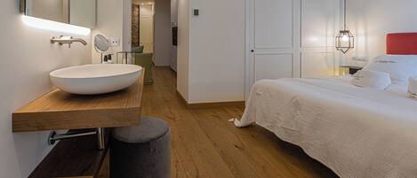 A modern bedroom with a large bed, a wooden vanity with a white sink, and a mirror.