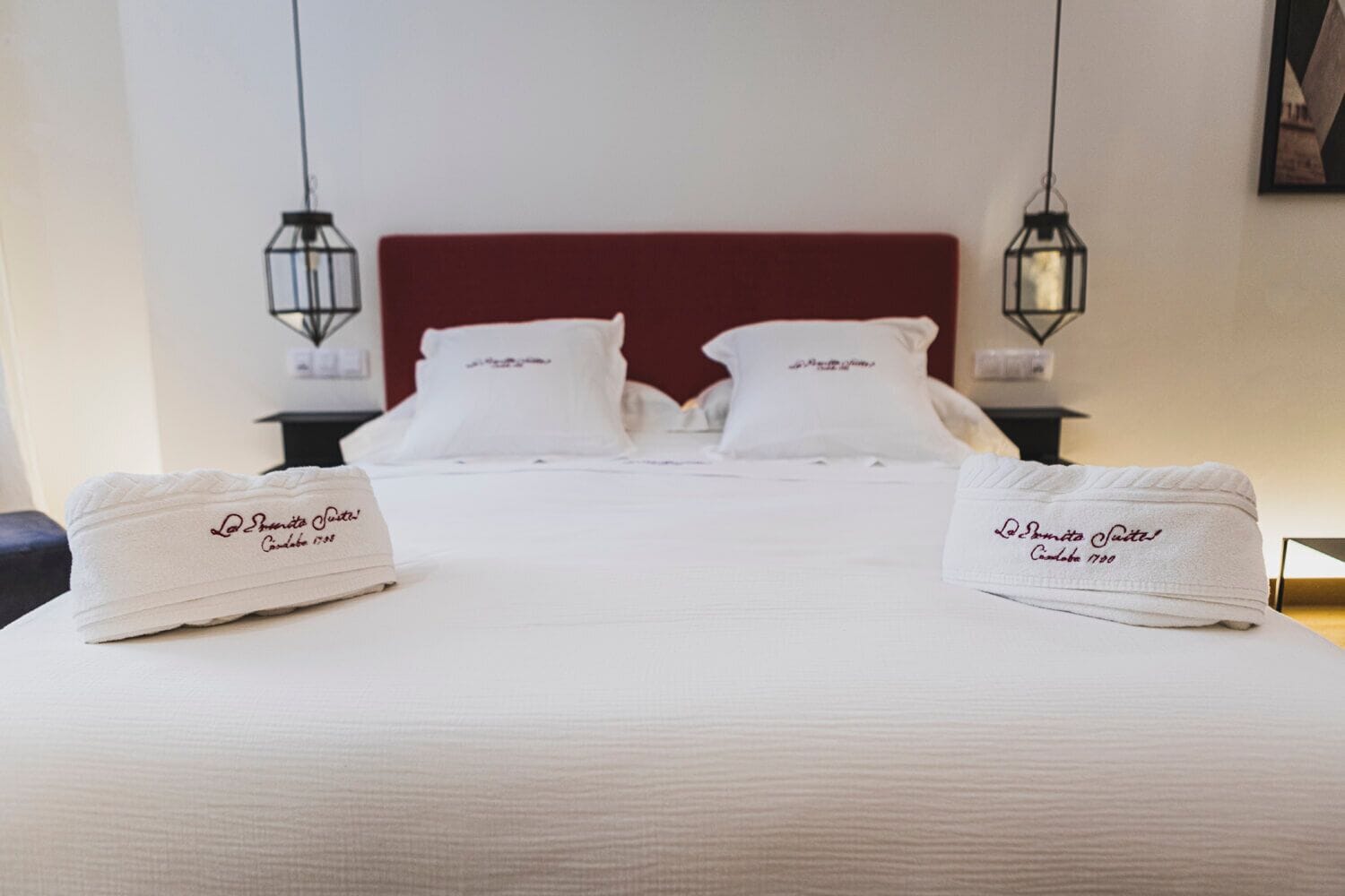 Habitación de hotel con una cama grande, dos mesitas de noche y dos lámparas colgantes.