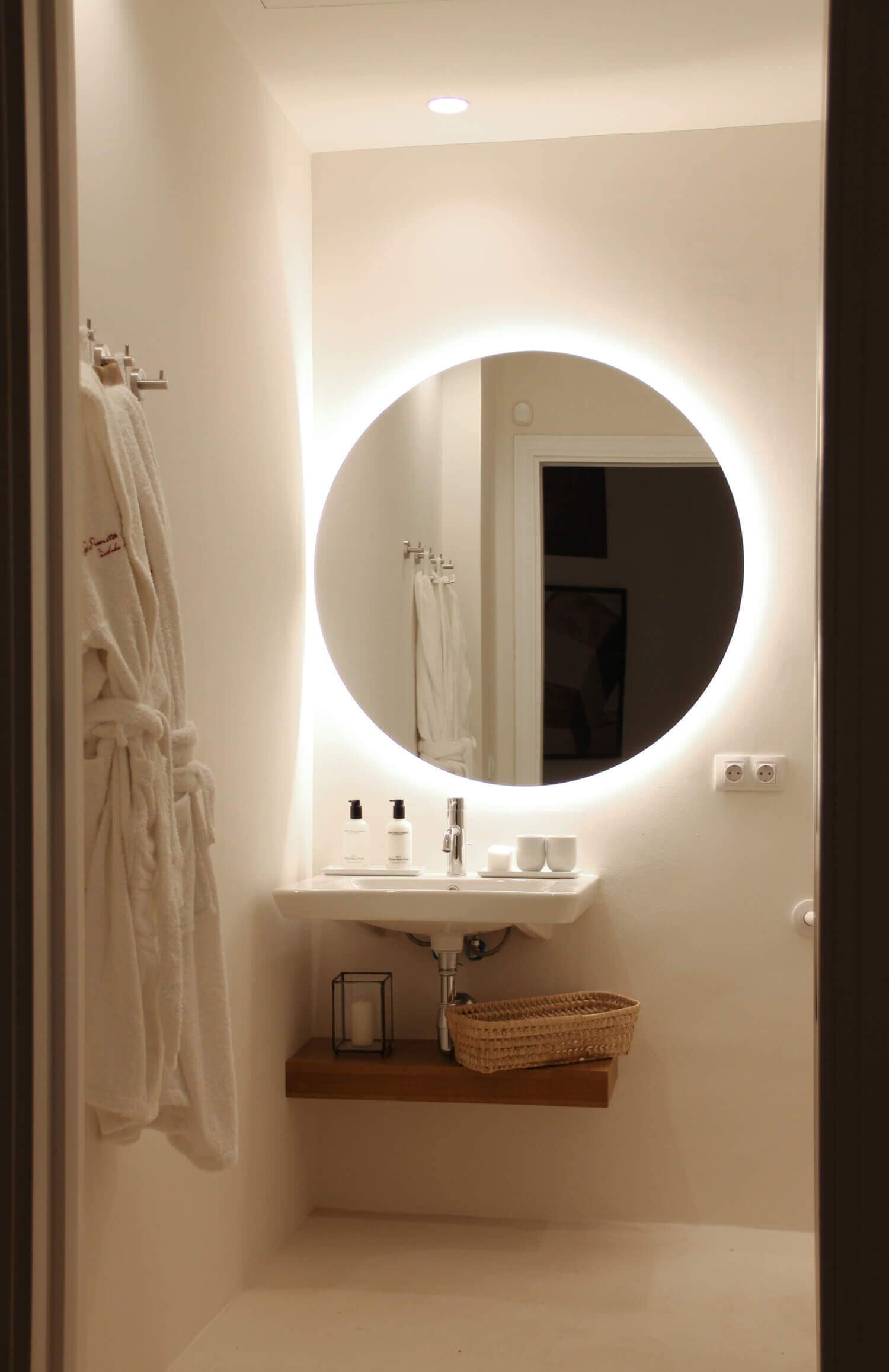 Ein Badezimmer mit rundem Spiegel, weißem Waschbecken und Handtuchhalter.