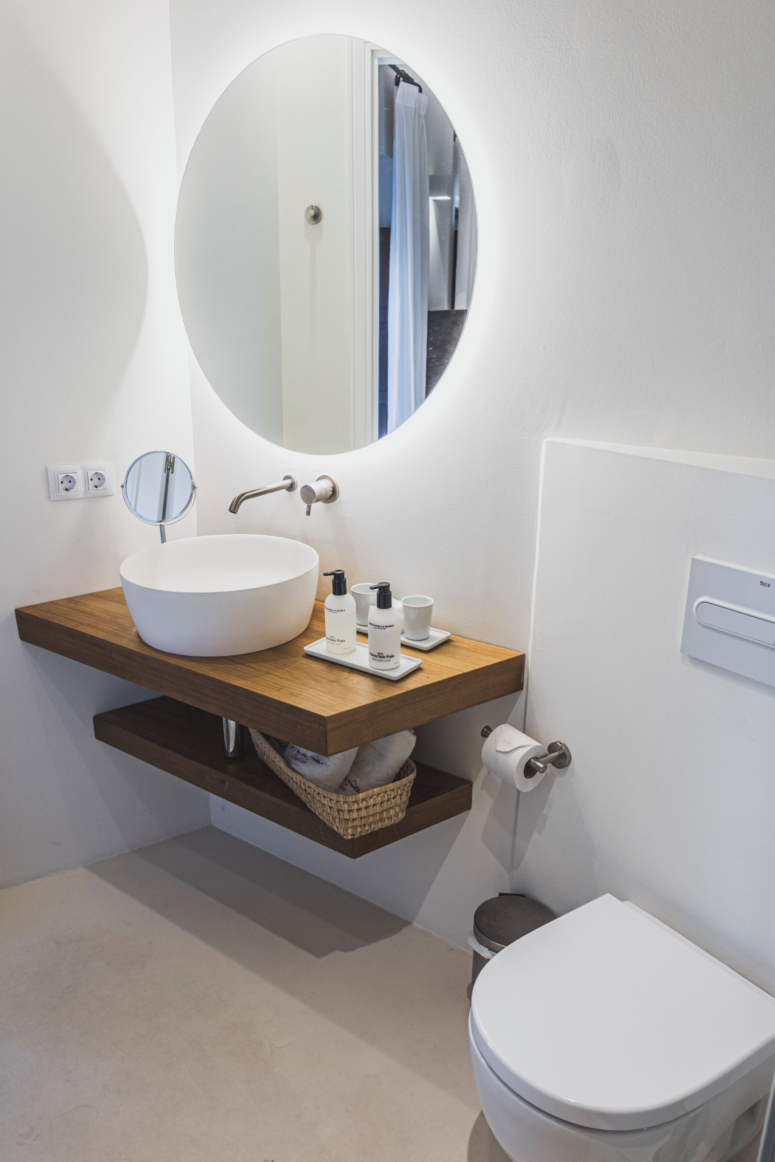 Un baño moderno con un espejo redondo, un lavabo blanco y un inodoro.
