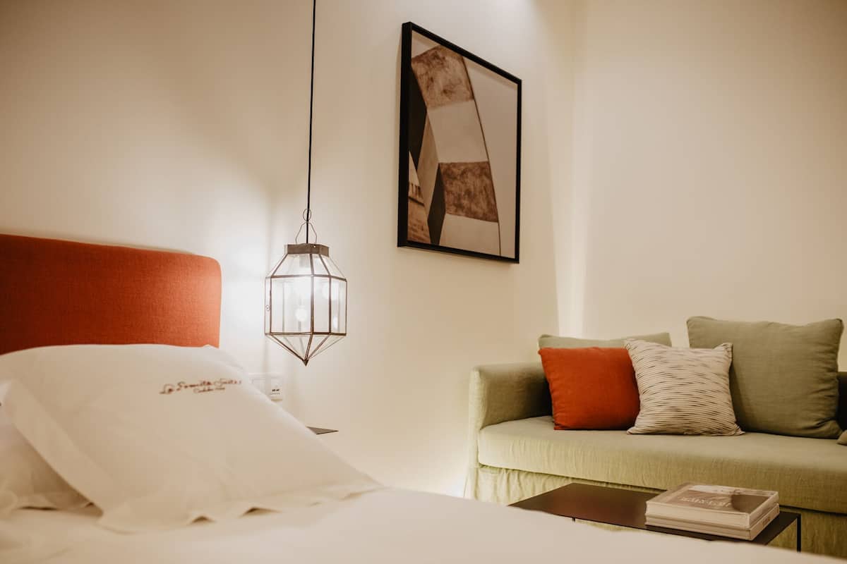 Una habitación de hotel con una cama, una lámpara colgante, un cuadro en la pared y un sofá con cojines.