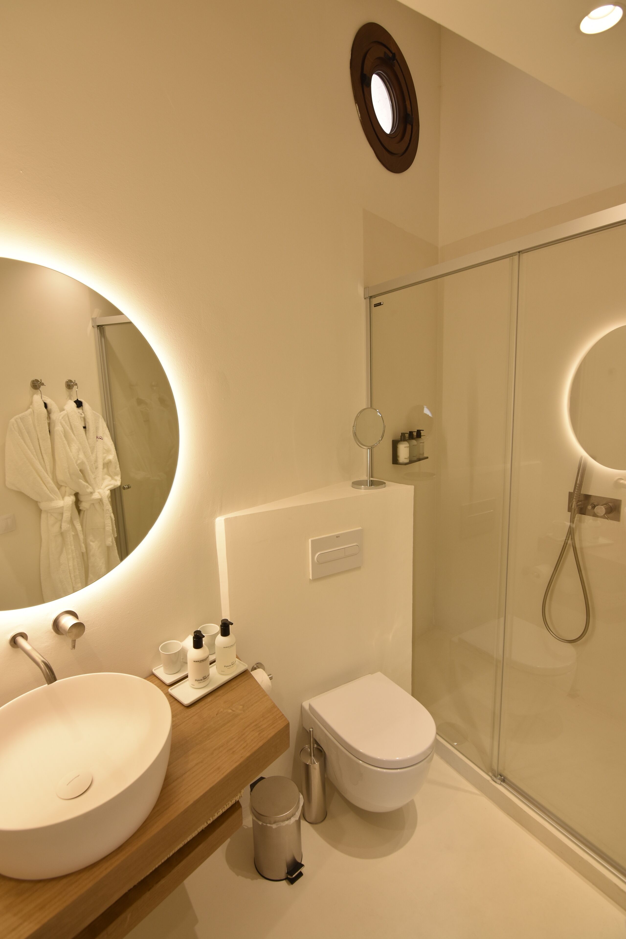 Un baño moderno con un lavamanos ovalado grande, un inodoro y una zona de ducha con mampara de vidrio.