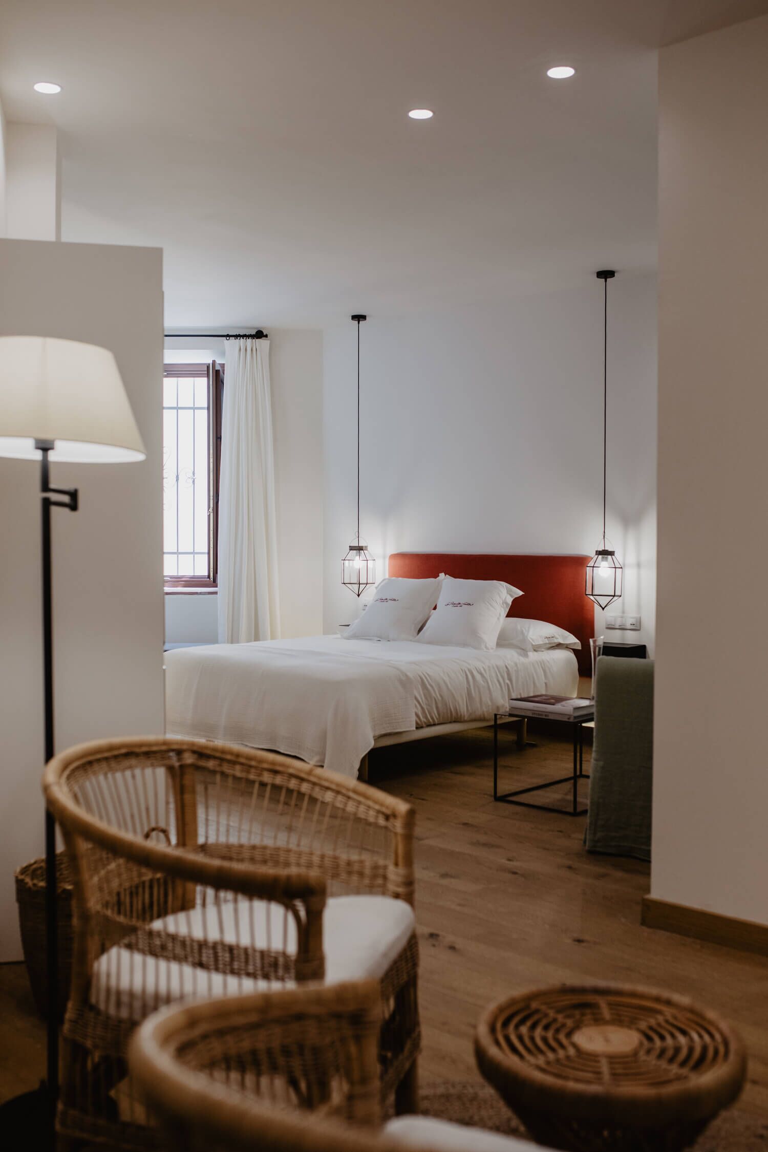 Hotellihuone, jossa on sänky, kaksi rottinkista tuolia, lattiavalaisin ja yöpöytä.