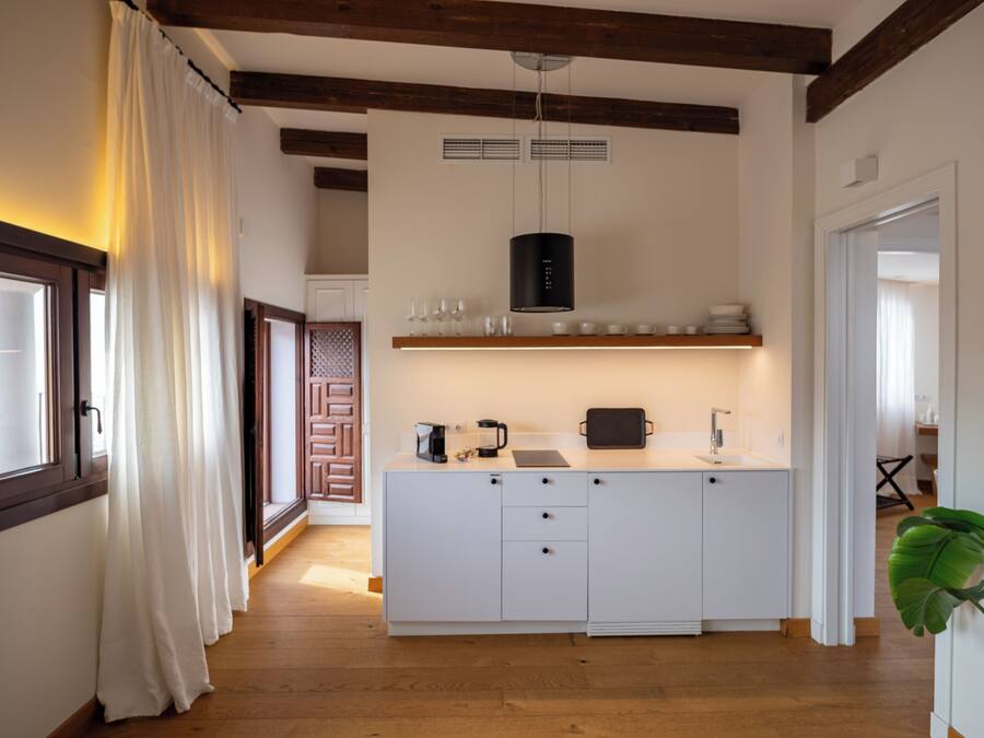 A modern kitchen with white cabinetry, a central island, a hanging light fixture, and a wooden ceiling.