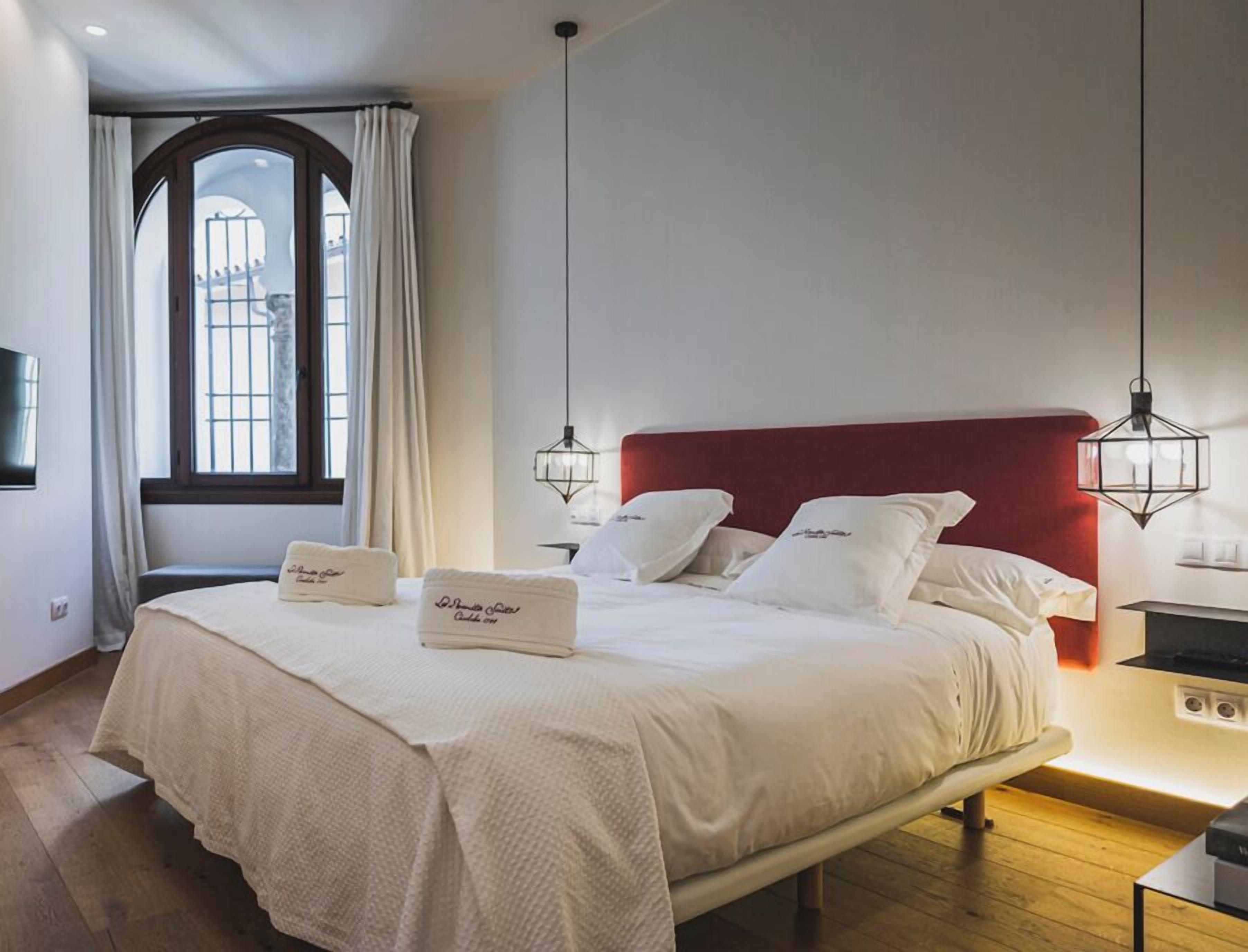 A neatly made bed with a red headboard, white bedding, and two bedside lamps.