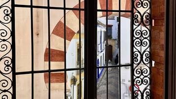 Vista a través de una ventana con rejas de hierro decorativas, mostrando una calle con edificios y un toldo rojo y blanco a rayas característico.