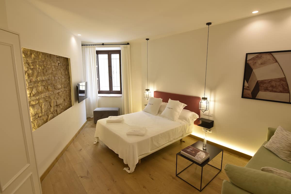 Un dormitorio con cama, mesitas de noche, un ventanal y un cuadro en la pared.