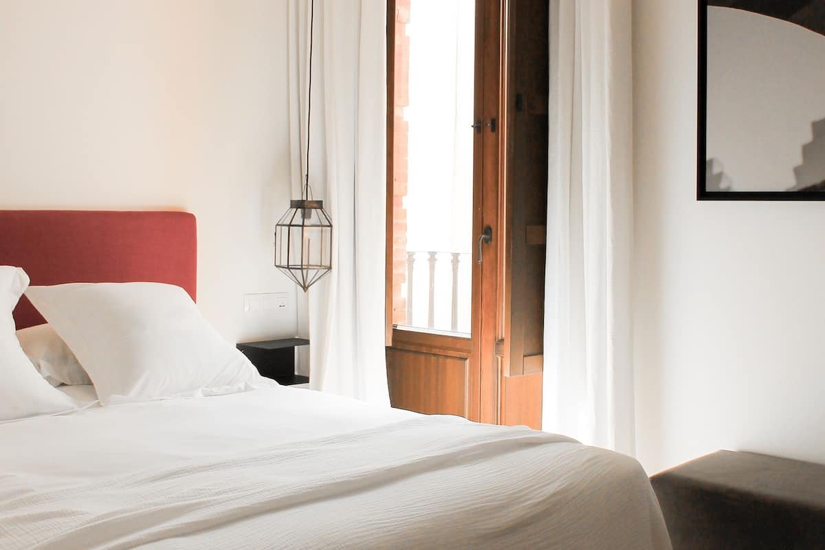 Un dormitorio con una cama, una mesita de noche, una lámpara colgante, una puerta y una vista parcial de un balcón.