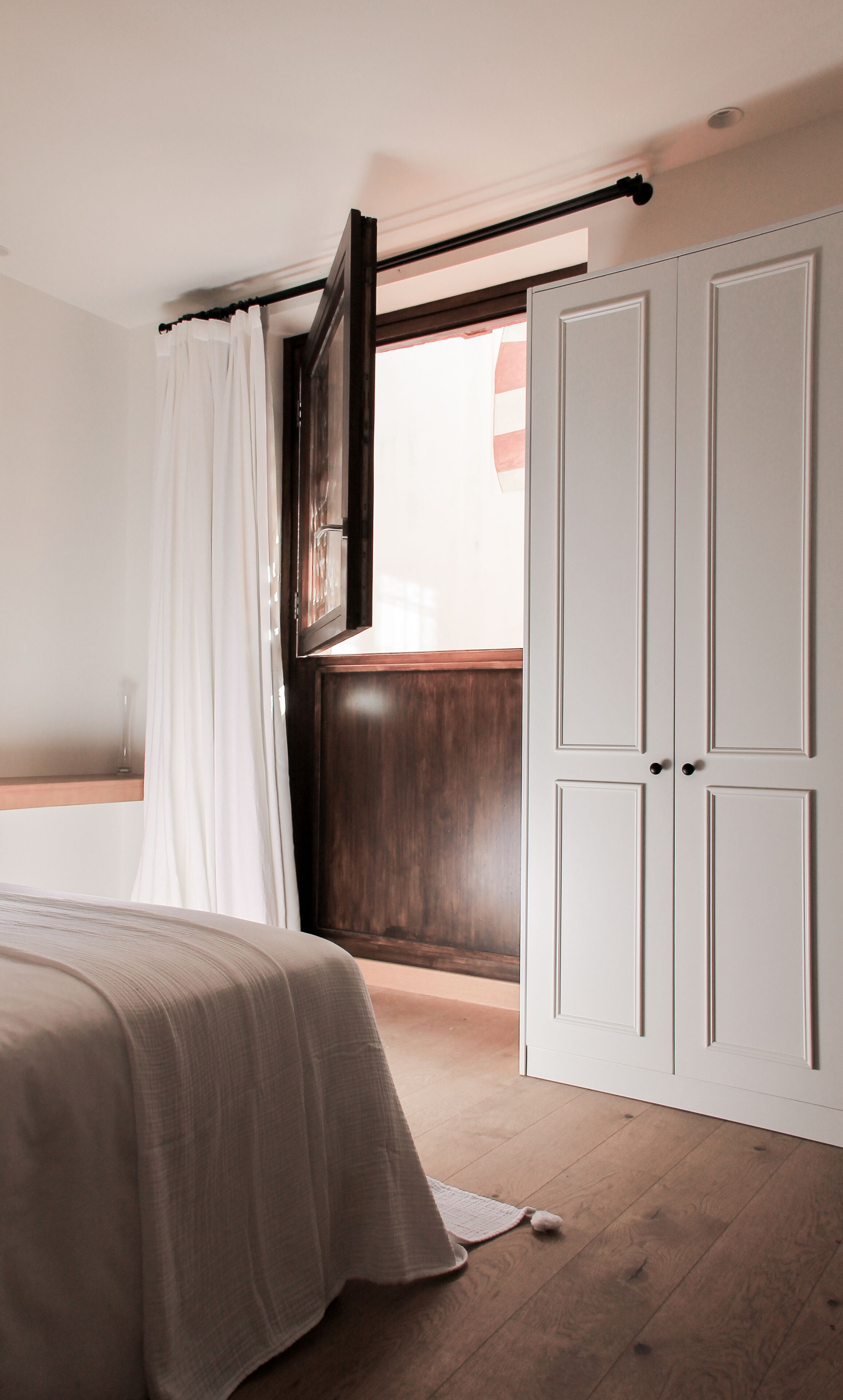 Un dormitorio con cama, armario de madera, ventana con cortinas y suelo de madera.
