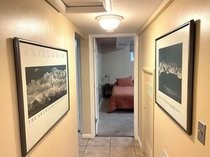 Ein Flur mit gerahmten Fotos an der Wand, ein Bett im angrenzenden Zimmer und eine Deckenleuchte.