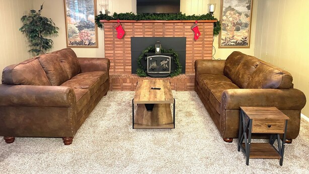 A living room with two leather sofas, a wooden coffee table, a fireplace with Christmas decorations, and framed artwork on the walls.