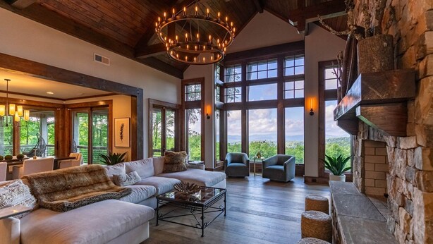 Un salón amplio con un sofá grande, dos sillones y una chimenea. La habitación cuenta con ventanas grandes que ofrecen vistas al exterior.