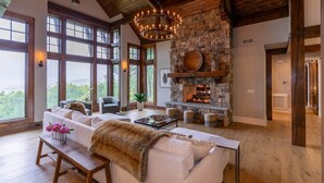 Un salón amplio con chimenea de piedra, ventanas grandes y un techo alto.