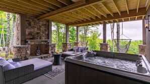 Un espacio al aire libre techado con paredes de piedra, un jacuzzi, muebles de mimbre y hamacas colgantes.