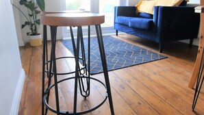 Et værelse med trægulv, et hvidt bord med metalstel, en blå sofa og et gult pled på sofaen.