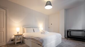 Et soveværelse med seng, natbord, lampe og et løbebånd.