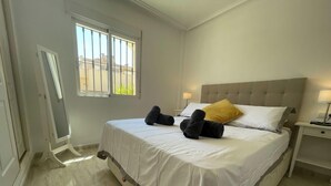 A bedroom with a bed, a nightstand, a window, and a door. - Sunny Brisa Golf II Retreat with Com Pools EB6 (Orihuela)