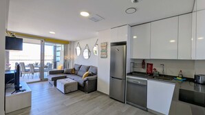 Eine moderne Küche mit Edelstahlgeräten, ein Essbereich mit Sofa und Tisch und ein großes Fenster, das für natürliches Licht sorgt.