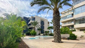 Ein modernes Gebäude mit Pool, Palmen und einer Bank.