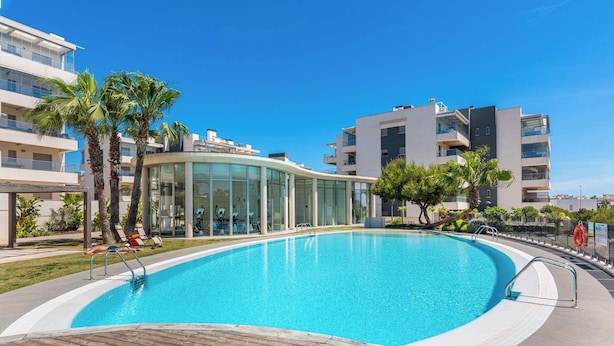 Ein modernes Hotel mit Schwimmbad, Palmen und einem Glasgebäude.