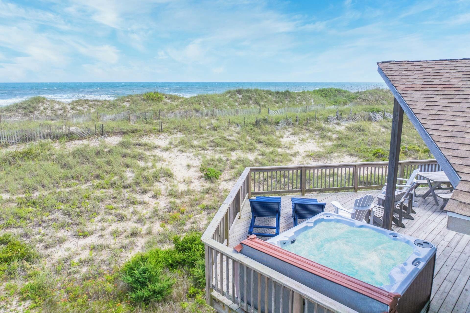 A wooden deck with a hot tub, lounge chairs, and a view of the beach and ocean.