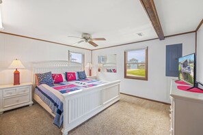 Un dormitorio con cama, dos mesitas de noche, ventilador de techo, ventana y espejo.