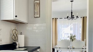 A modern kitchen with white cabinetry, a black countertop, and a dining area with white chairs and a chandelier. - The Chic Shack | Centrally Located 2BR/1BA Home (Evansville)
