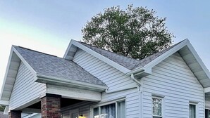 A two-story house with a brick foundation, a front porch, and a small front yard. - The Chic Shack | Centrally Located 2BR/1BA Home (Evansville)