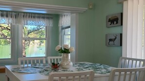 A dining area with a table set for four, a vase with flowers, and two animal-themed wall art pieces. -  Charming  Cozy  Waterfront Cottage  (Val Des Bois)